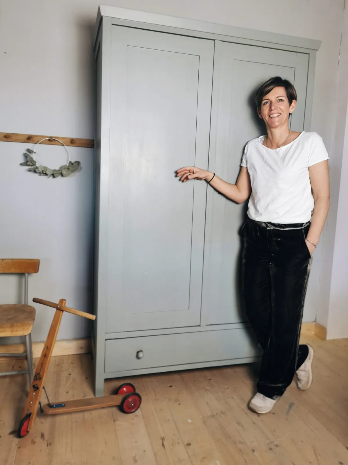 Katrina Gietl steht neben einem hellgrau aufgearbeiteten Kasten, daneben ein alter Tretroller und ein Schulsessel