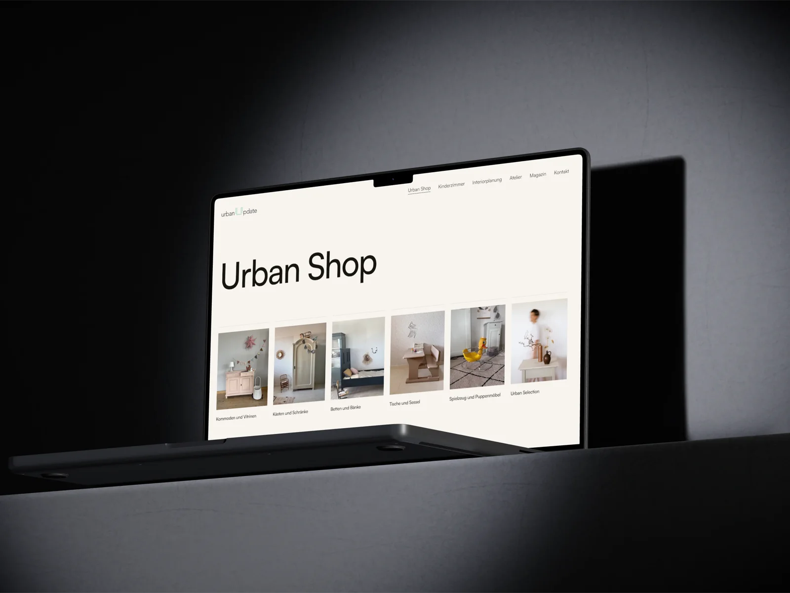 Ein aufgeklapptes MacBook vor dunkler Wand, auf dem Bildschirm der Urban Shop mit den sechs Kategorien
